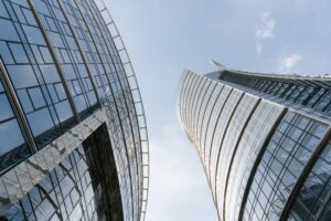 Upward view between two modern glass skyscrapers against a blue sky.